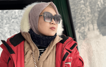 Kabin Kashmir Gondola Ride melayang di atas pegunungan bersalju Gulmarg dengan pemandangan lembah hijau dan Himalaya.