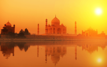 Pemandangan Taj Mahal dengan kubah marmer putih dan menara, dikelilingi taman hijau.